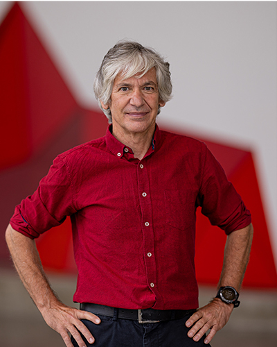 Un homme souriant, portant une chemise rouge, se tient debout avec assurance devant un fond géométrique rouge.