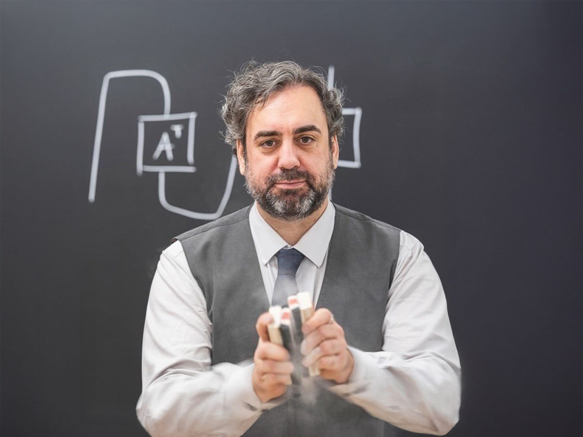 An instructor demonstrates teaching concepts in a classroom, surrounded by educational tools and a chalkboard.