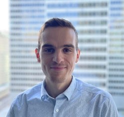 Étudiant souriant en technologie, il se tient devant une vue urbaine moderne, reflétant une ambiance dynamique et professionnelle.