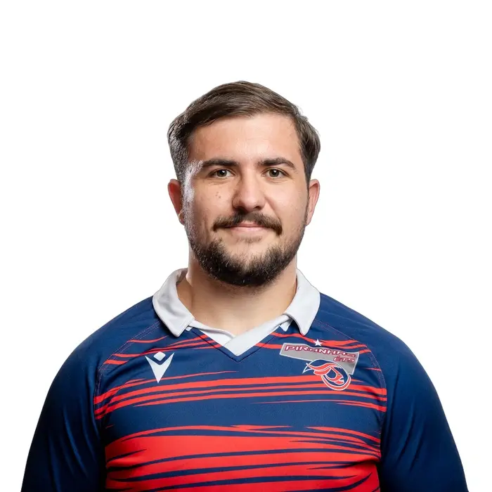 Jeune homme souriant portant un maillot de rugby aux couleurs vives, affichant fierté et détermination.