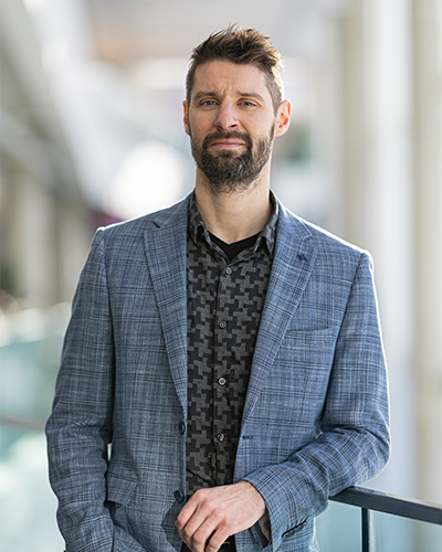 Un professionnel en tenue soignée se tient décontracté dans un environnement moderne, dégageant confiance et ouverture.