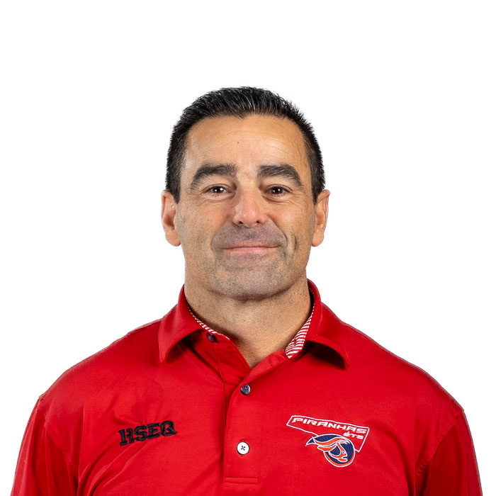 Professeur en technologie, chemise rouge avec logo d'équipe, souriant, fond blanc.