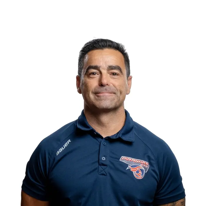 Professeur en technologie, chemise rouge avec logo d'équipe, souriant, fond blanc.