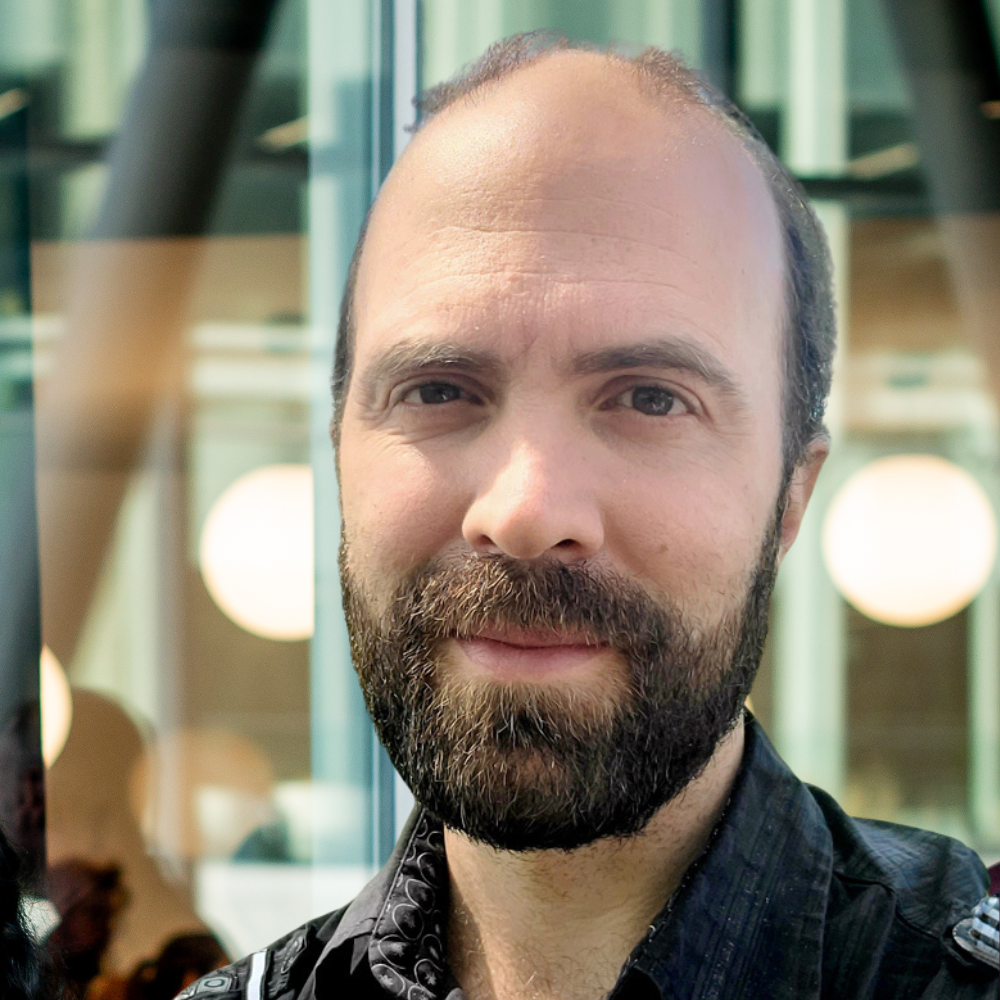 A smiling man with a beard stands in a modern environment, showcasing a blend of professionalism and approachability.