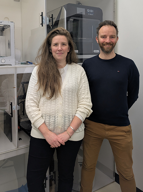 Two people standing in a 3D printing laboratory, surrounded by modern technological equipment.