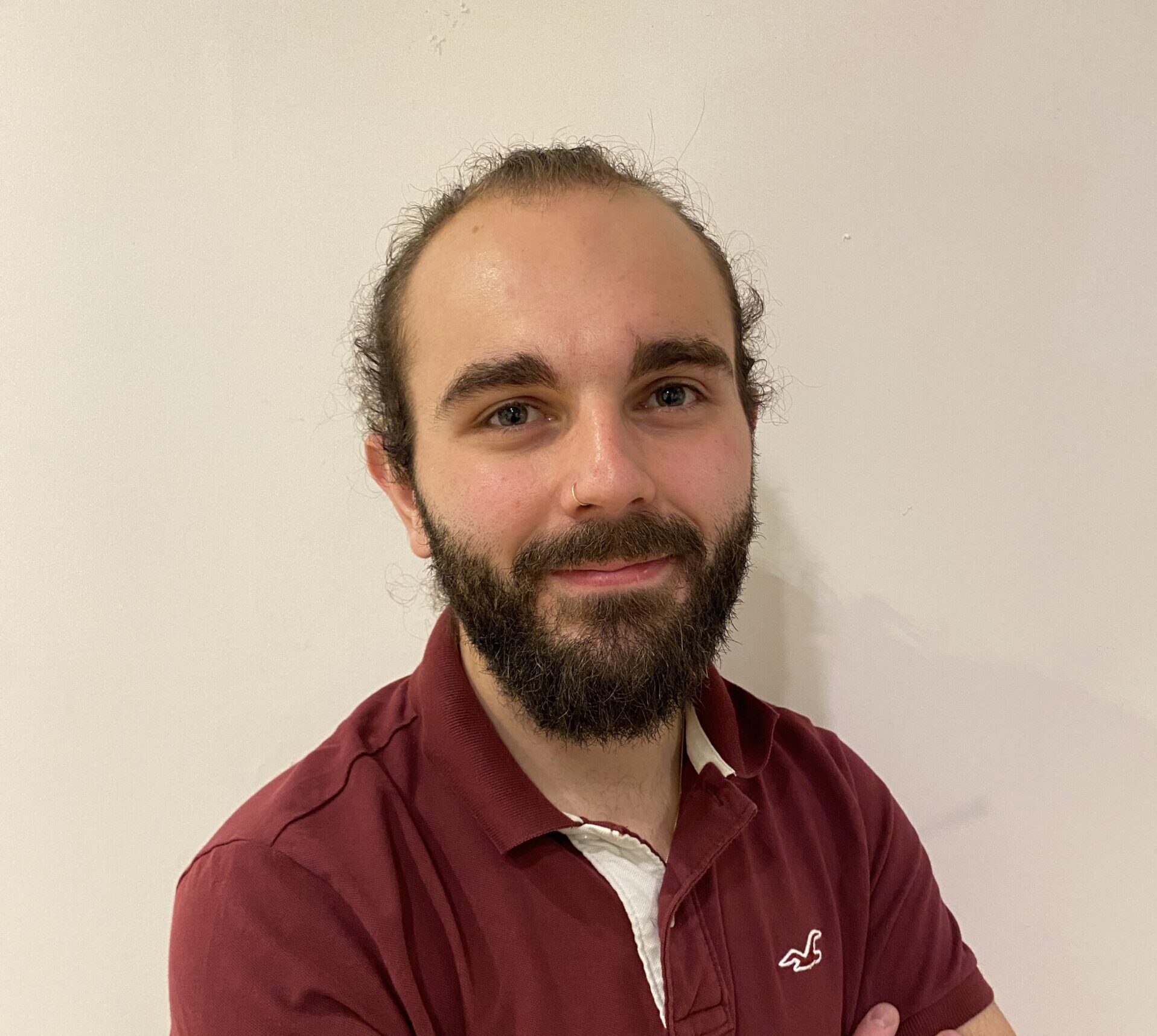 Étudiant en technologie, souriant et confiant, il présente une allure décontractée avec une barbe bien entretenue.