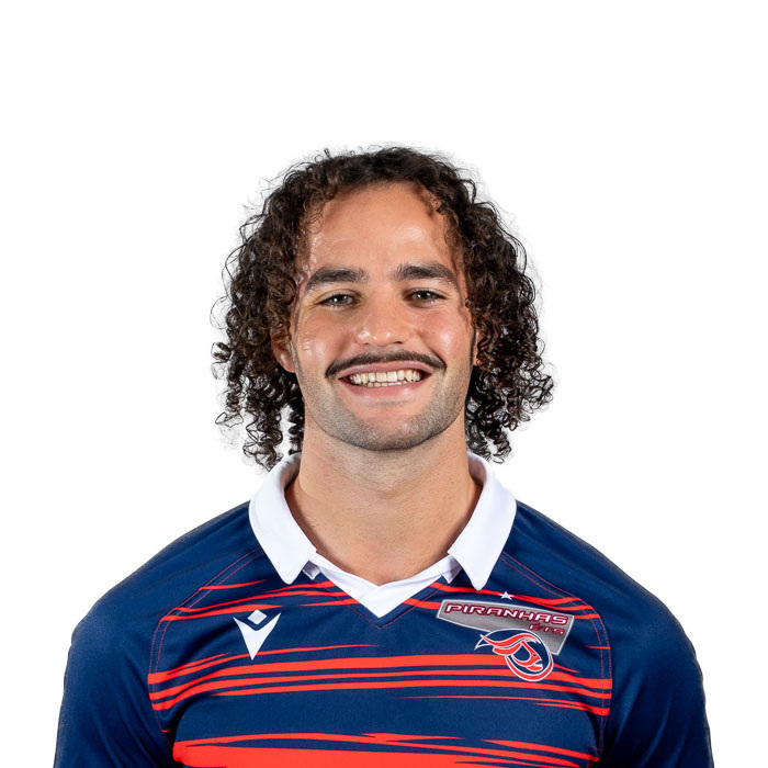 Étudiant souriant, cheveux bouclés, portant un maillot sportif bleu avec des bordures rouges.