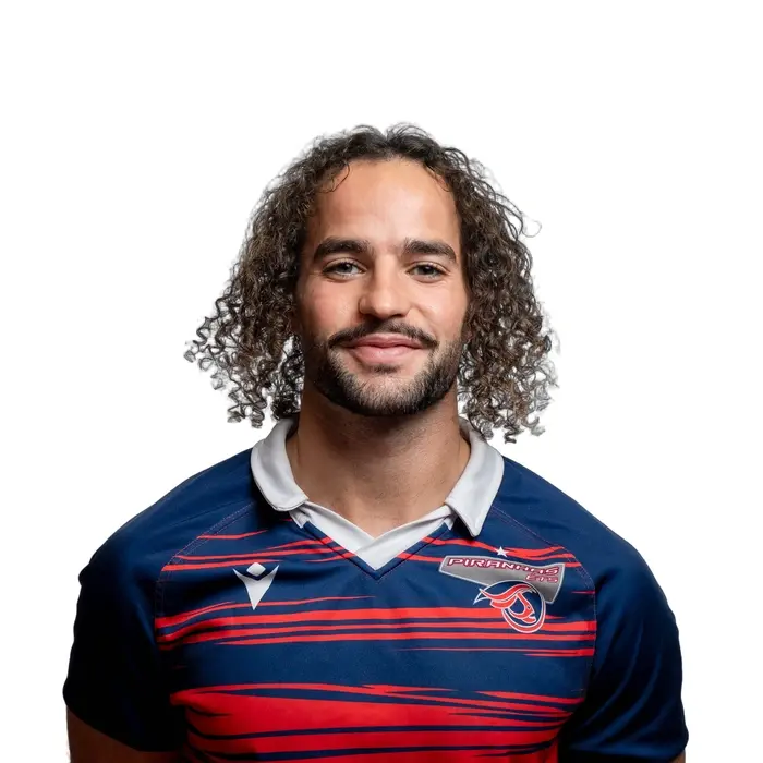 Étudiant souriant, cheveux bouclés, portant un maillot sportif bleu avec des bordures rouges.