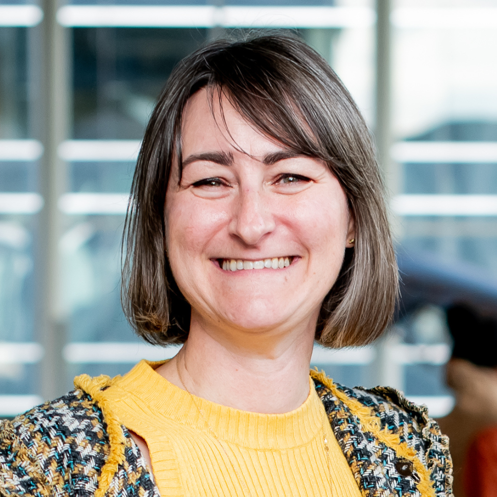 A smiling individual with short hair, wearing a colorful sweater and yellow top, exemplifying a welcoming and vibrant atmosphere.