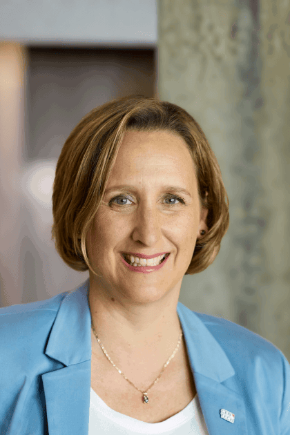 Portrait d’une femme souriante, regard face caméra, portant un veston bleu dans un environnement intérieur.