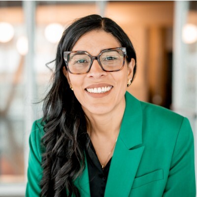 Professionnelle souriante, portant une veste verte, elle incarne le dynamisme et l'enthousiasme dans un environnement collaboratif.