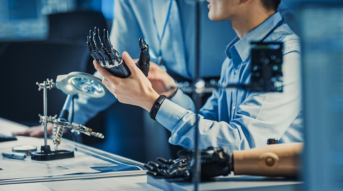 Étudiants en ingénierie examinant une main robotique prothétique.