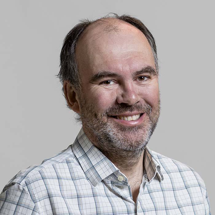Friendly professor with a welcoming smile, wearing a plaid shirt.