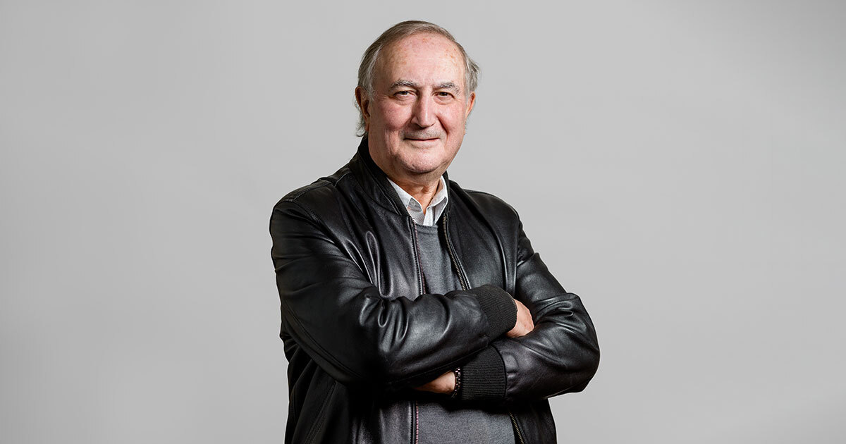 A distinguished professor in technology, exuding confidence with crossed arms and a warm smile against a neutral backdrop.