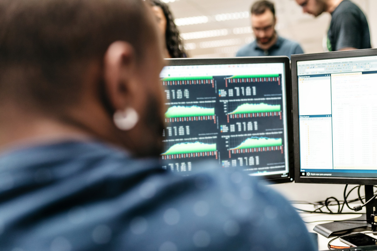 A student analyzes data on multiple monitors, focused on graphs and statistics in a collaborative tech environment.