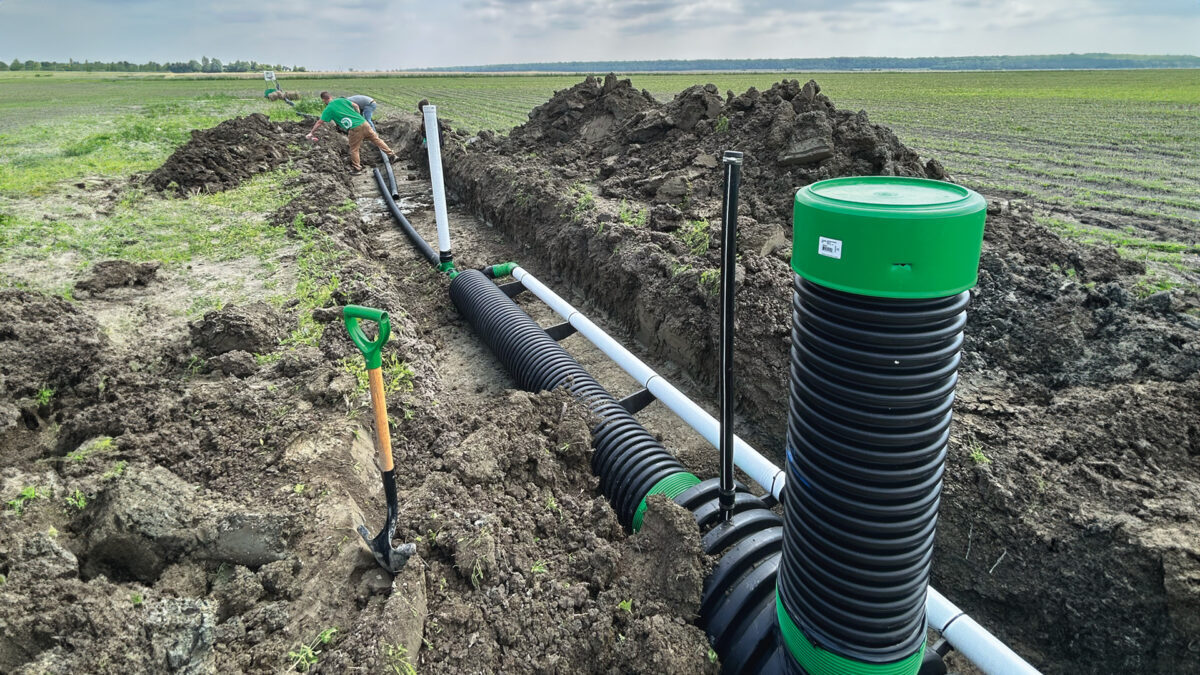 Travaux d'installation de systèmes de drainage, avec un ouvrier à l'extérieur, sur un terrain agricole. Terre retournée et canalisations en place.
