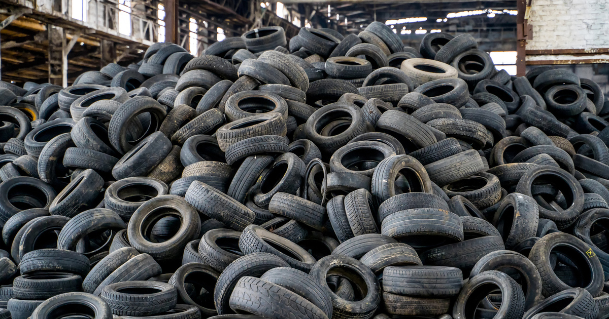 A large, chaotic pile of used tires fills an industrial space, reflecting challenges of waste management and recycling in urban environments.