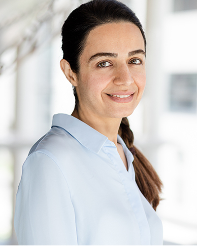 Portrait d'une femme souriante, portant une chemise bleue, dans un environnement lumineux et moderne. Émanation de confiance et de professionnalisme.
