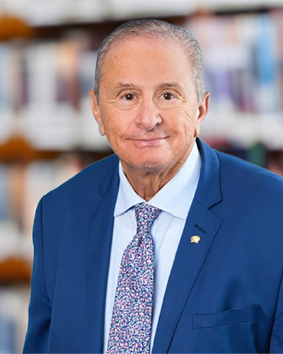 Un homme souriant, en costume bleu, se tient devant une bibliothèque, reflétant un environnement académique chaleureux et accueillant.