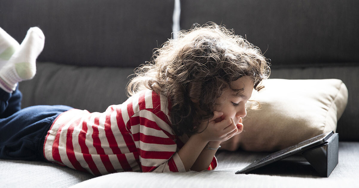 Un enfant curieux explore un contenu numérique, allongé sur un canapé, captivé par un appareil. Une scène de découverte moderne.