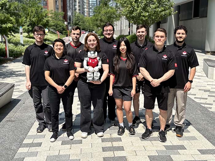 Équipe enthousiaste en tenue noire, réunie dans un espace urbain, présentant un robot. Ambiance collaborative et innovante.