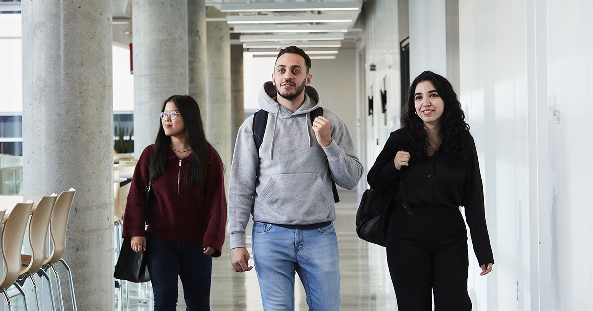 Trois étudiants se déplacent avec assurance dans un couloir moderne, illustrant la vie dynamique de l'université.
