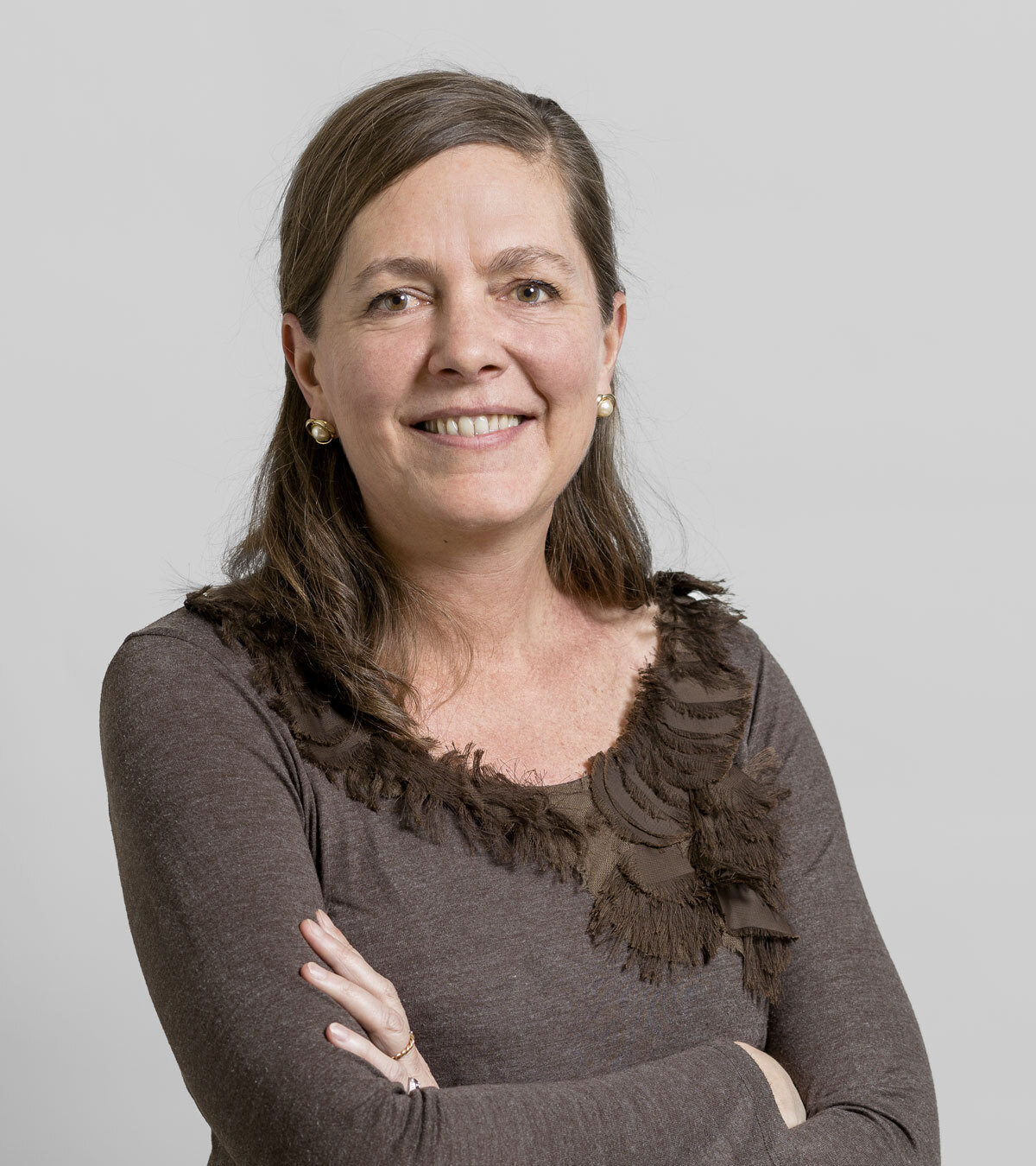 Portrait d'une femme au sourire chaleureux, arborant un haut brun avec des détails en tissu, sur fond neutre.