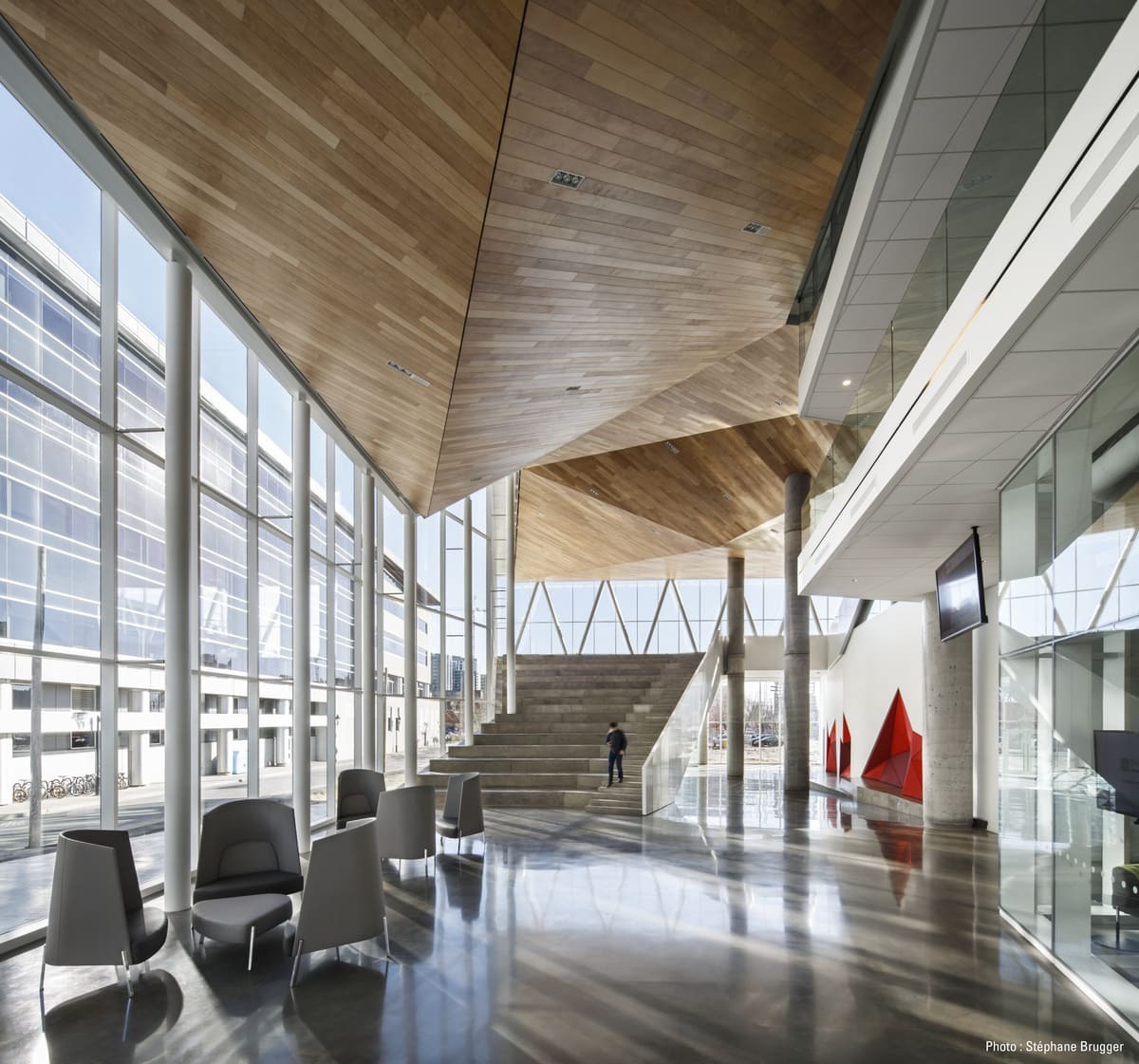 Espace moderne avec de grandes fenêtres, un plafond en bois et des zones de détente, favorisant un environnement d'apprentissage inspirant.