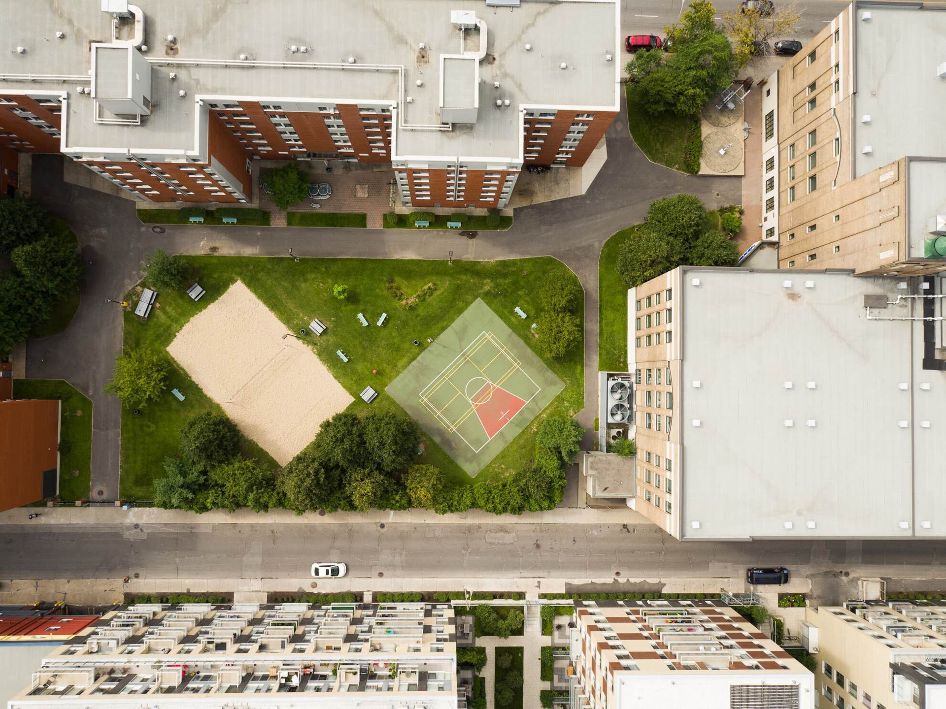 Vue aérienne d'un campus étudiant, avec des immeubles entourant des espaces verts, un terrain de basketball et un sable de plage.
