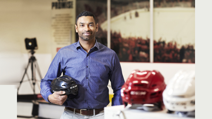 Un homme pose avec un casque de hockey dans un environnement technologique, symbolisant l'innovation et l'éducation supérieure.