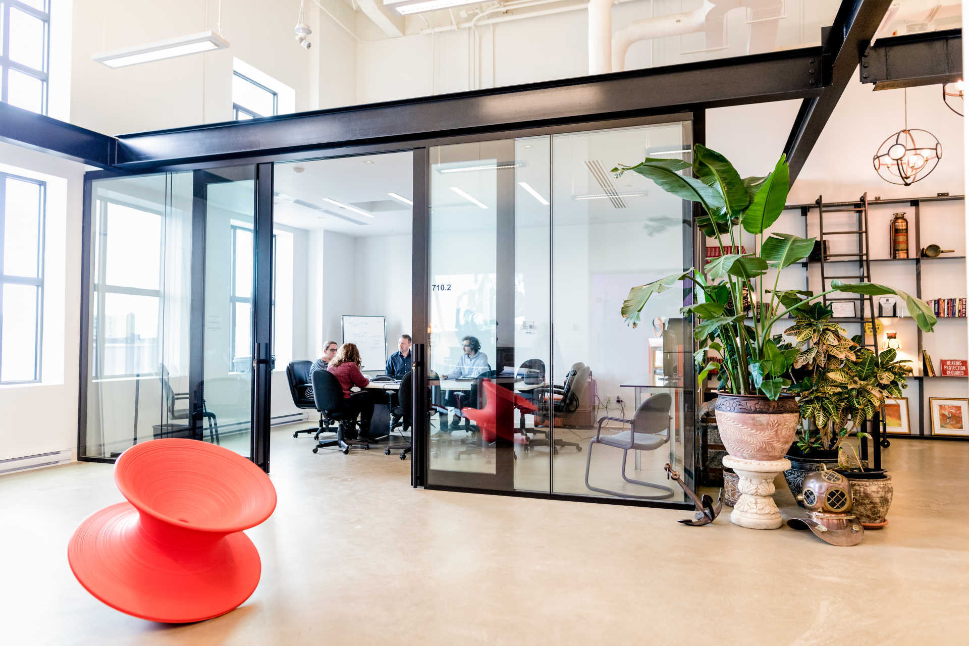 Modern workspace featuring a glass meeting room, vibrant decor, and greenery, promoting collaboration and creativity.
