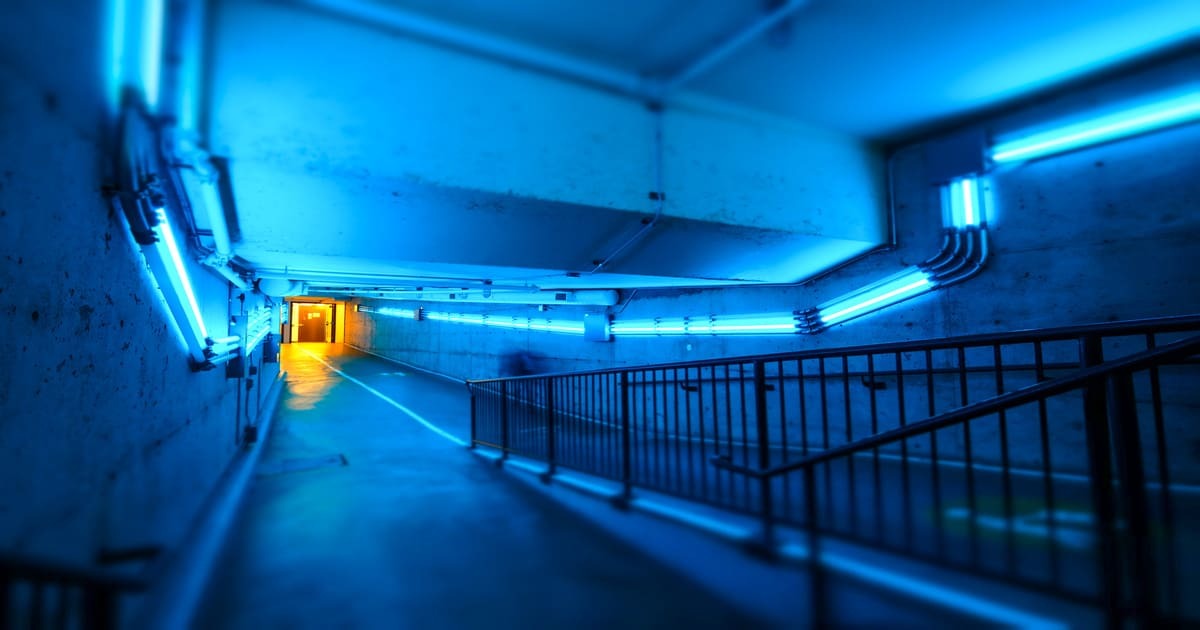 Un couloir dimly lit avec des néons bleus crée une atmosphère futuriste, menant vers une porte illuminée au loin.