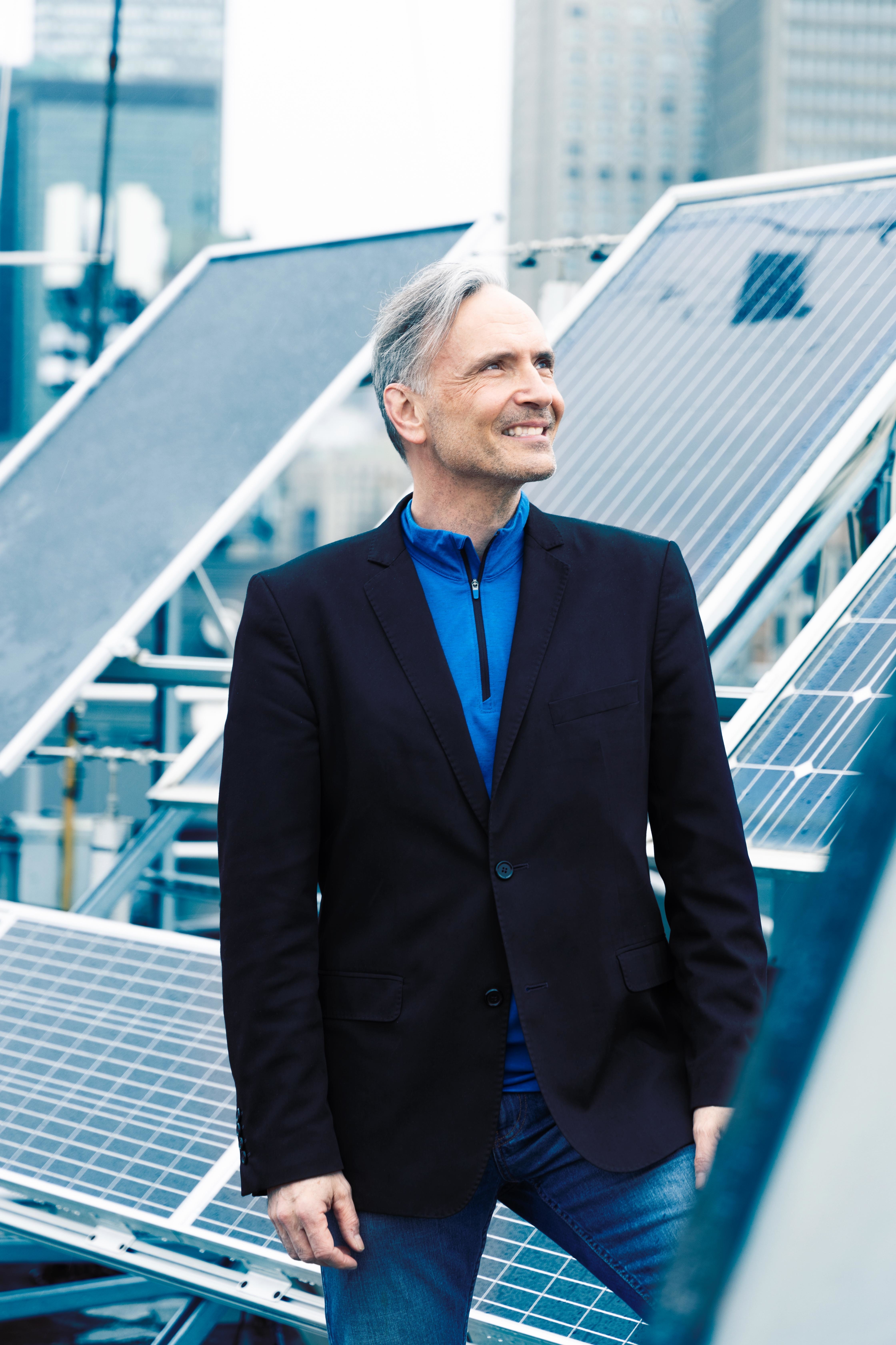 Un homme souriant se tient près de panneaux solaires, symbolisant l'innovation et l'engagement envers les énergies renouvelables.