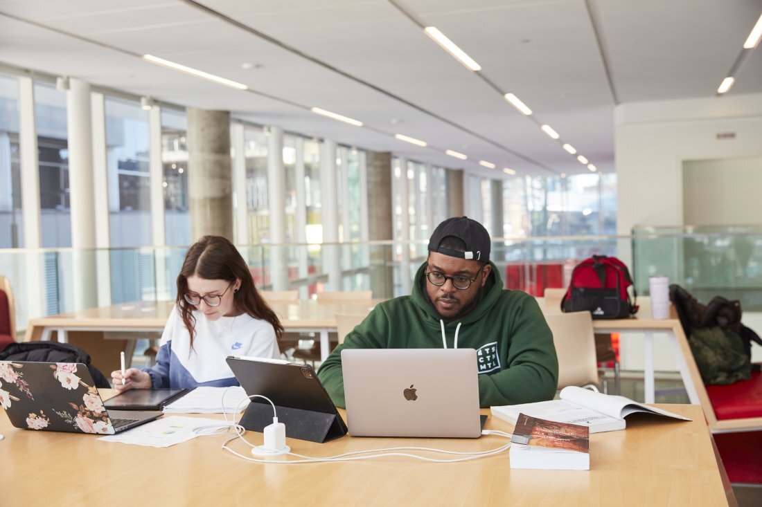 Des étudiants concentrés travaillent ensemble dans un espace moderne, entourés de technologies et de livres.