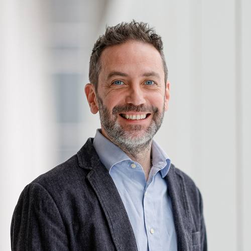 Un professeur charismatique, souriant, dans un environnement moderne d'enseignement supérieur, reflétant expertise et accessibilité.