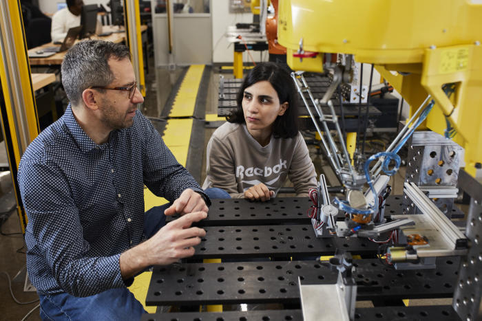 Un enseignant et une étudiante collaborent sur un projet de robotique, partageant des idées dans un environnement technologique.