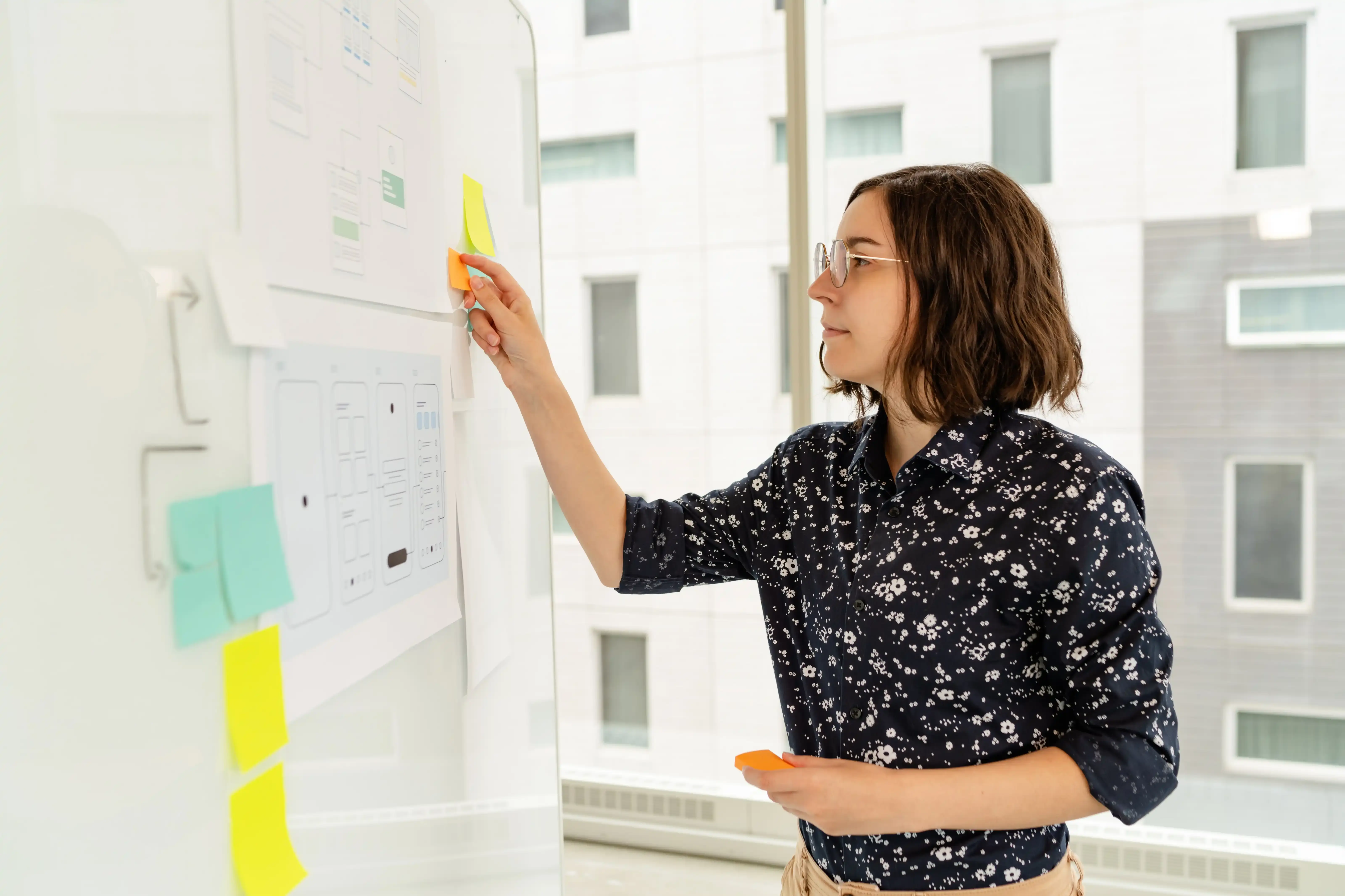 Femme collant des notes adhésives sur un tableau blanc lors d'un atelier de design UX.