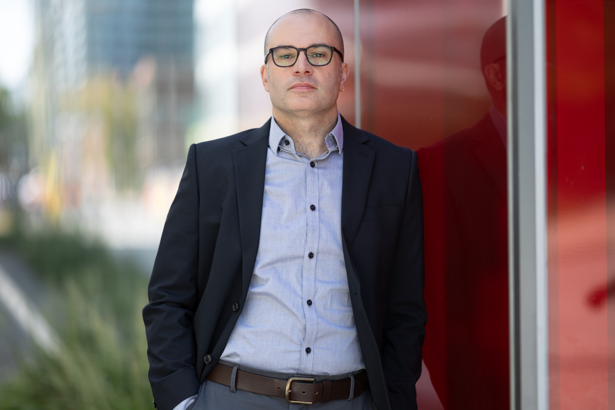 Professor in business attire with glasses, standing confidently outdoors.