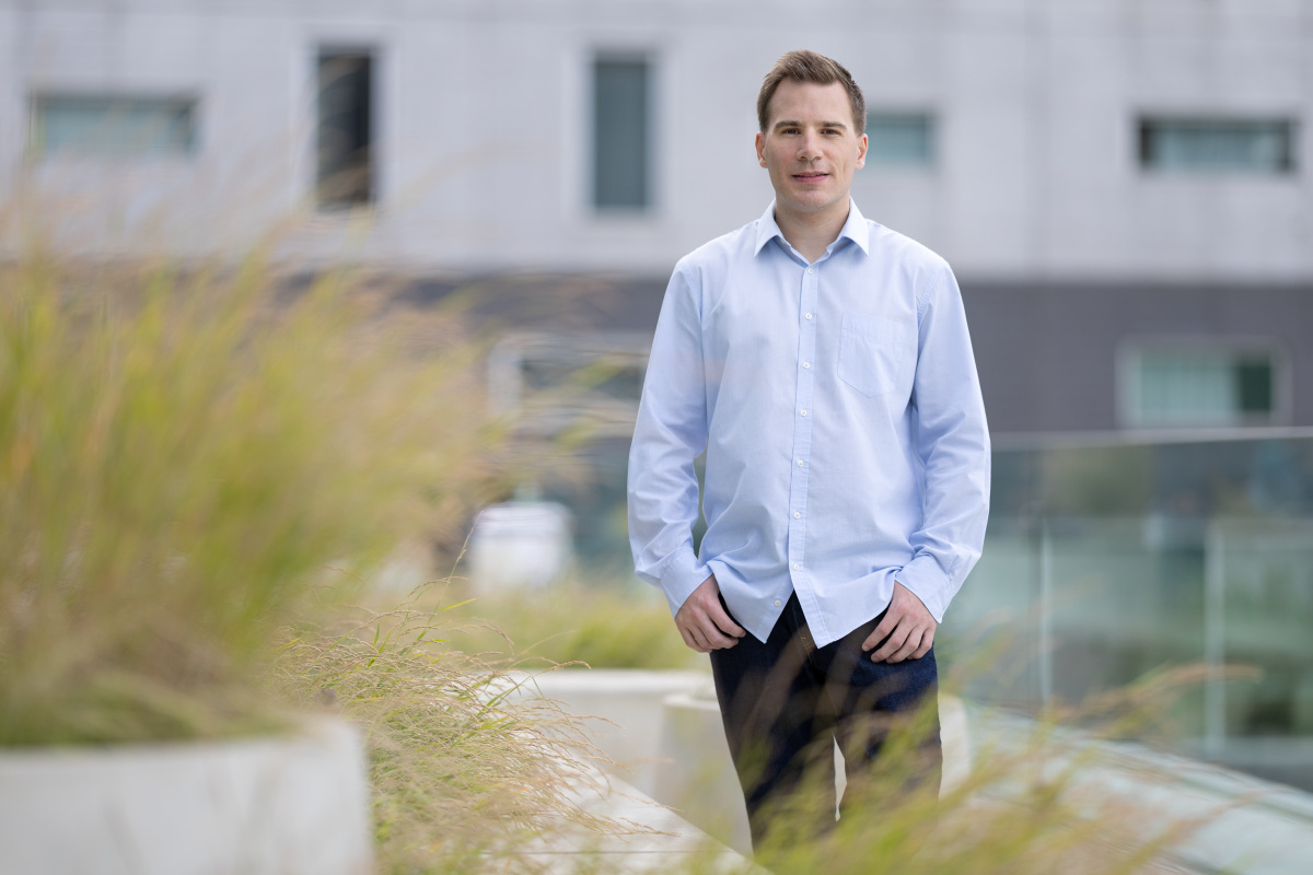 Professional in a blue shirt standing before a modern university building.