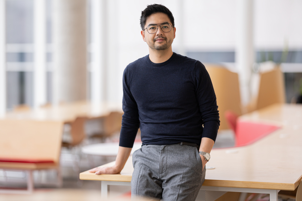 A confident individual stands casually in a modern, well-lit workspace, showcasing academic engagement and innovation.