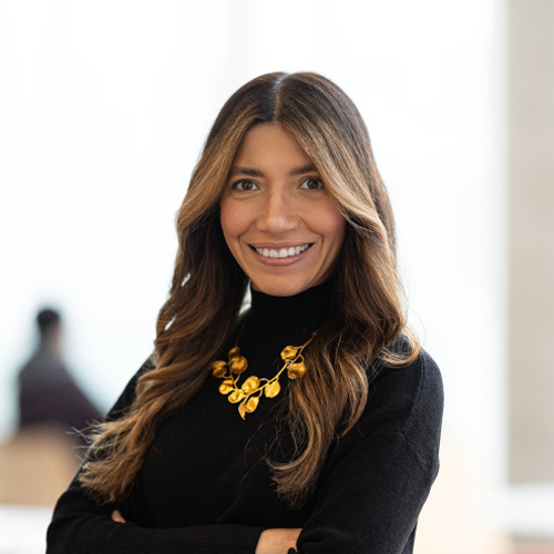 Portrait d'une professionnelle souriante en pull noir, avec un collier doré, symbolisant l'innovation et l'engagement dans l'enseignement supérieur.
