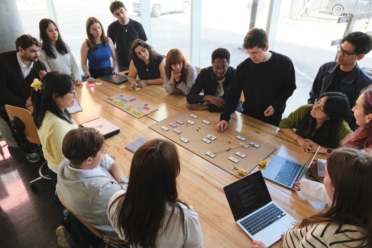 Un groupe d'étudiants collabore autour d'une table, échangeant des idées et travaillant sur un projet avec des ordinateurs portables et des notes.