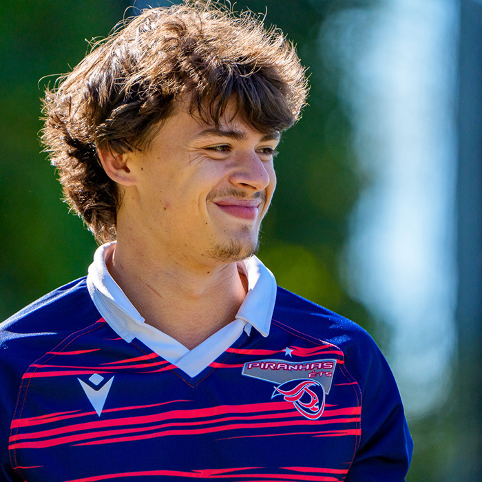Un jeune homme souriant porte un maillot de rugby aux couleurs vibrantes, captivant l’attention par son enthousiasme.