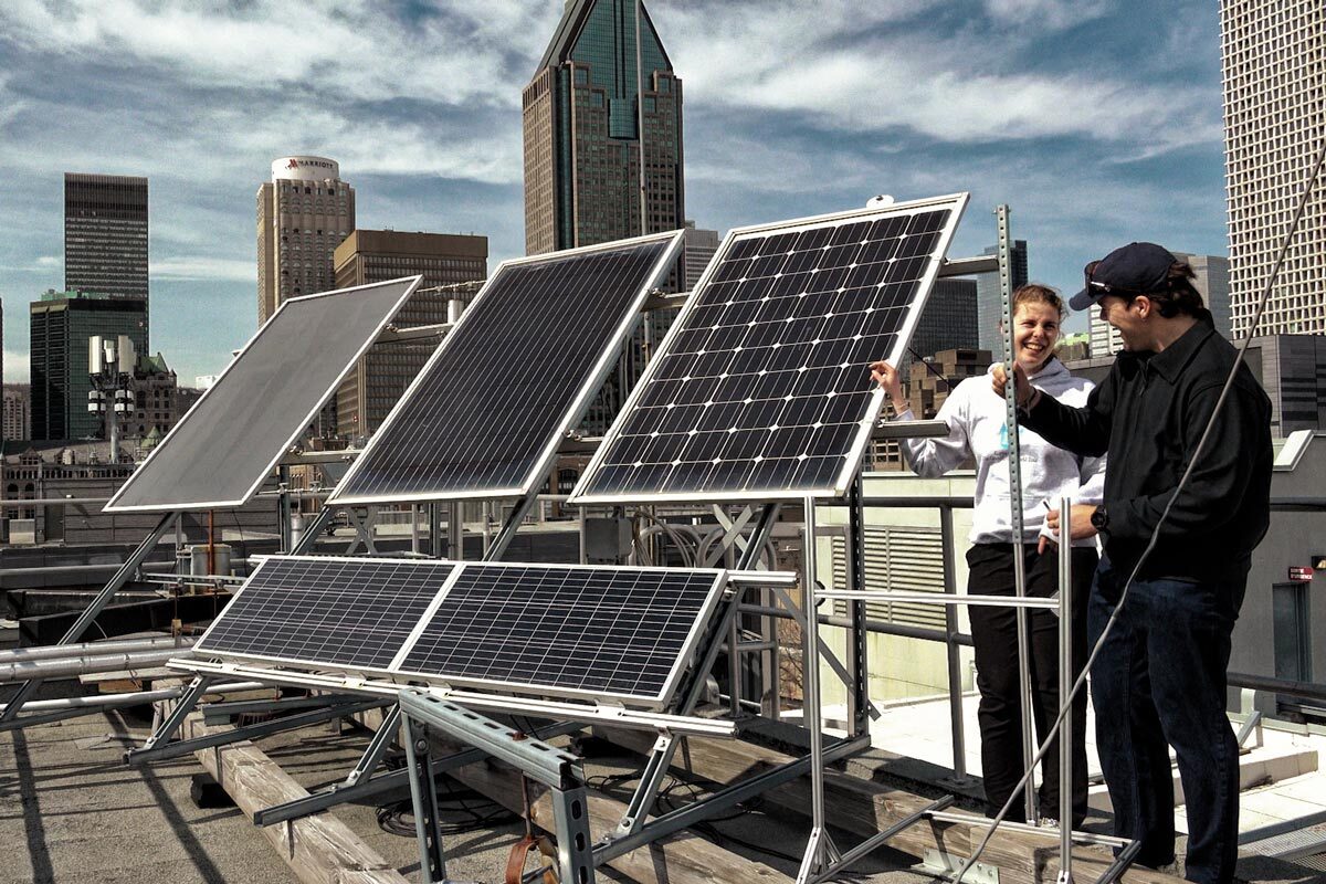 Des étudiants échangent des idées sur un système de panneaux solaires, sur le toit d'un bâtiment en milieu urbain, sous un ciel ensoleillé.