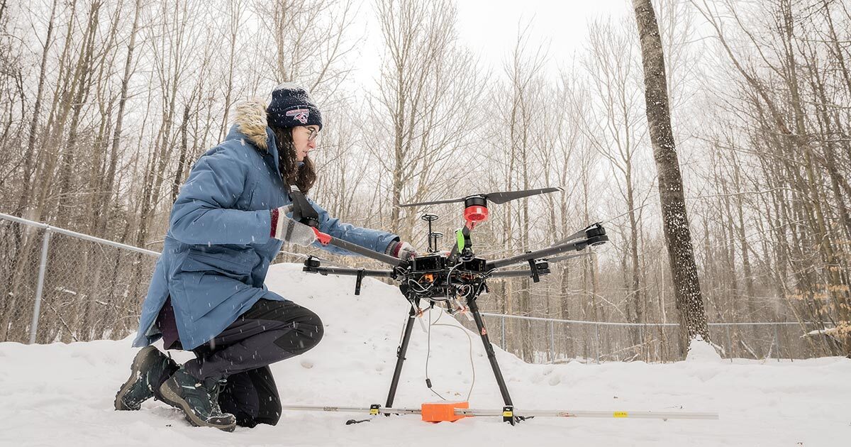 Une étudiante ajuste un drone en hiver, dans un environnement enneigé, illustrant l'innovation technologique et la recherche en plein air.