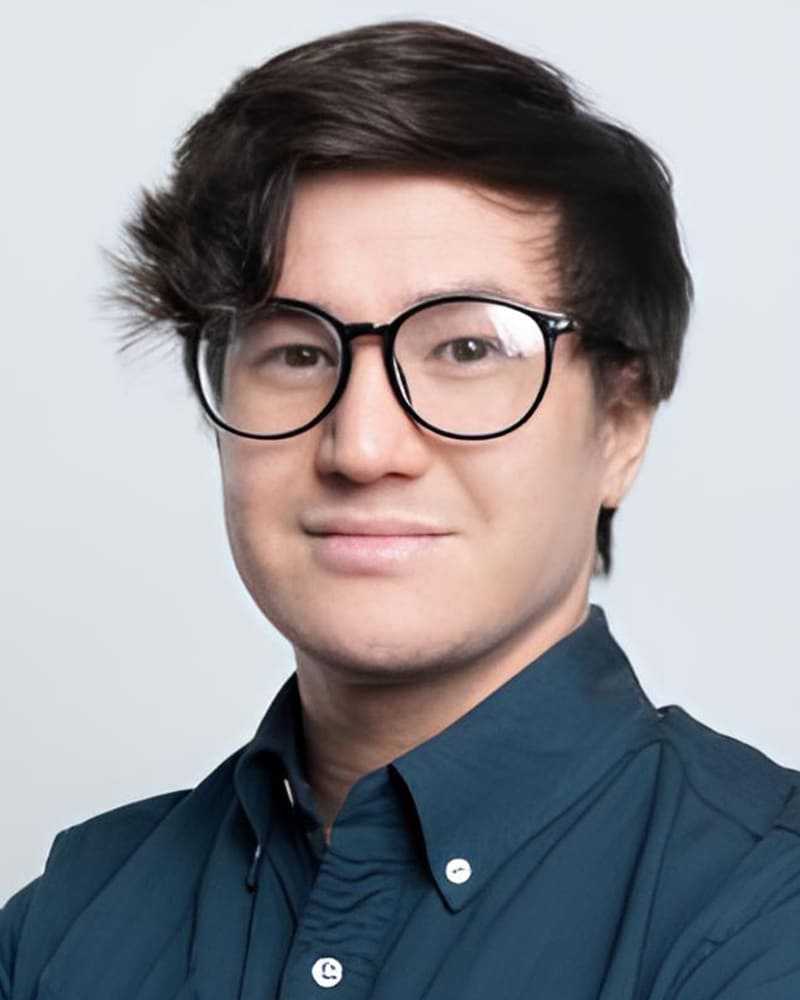 Personne portant des lunettes avec un sourire amical, vêtue d'une chemise bleue, devant un fond neutre.