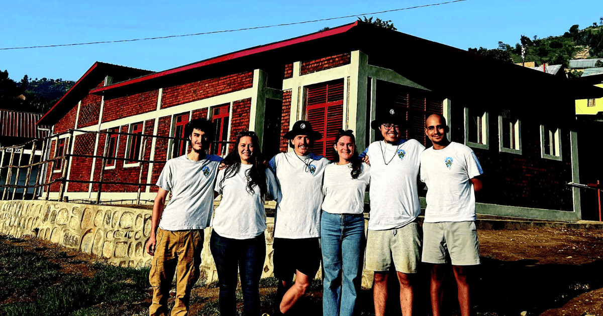 Un groupe d'étudiants posant ensemble devant un bâtiment. Ils sourient, vêtus de t-shirts identiques, sous un ciel clair.