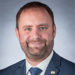 Un homme souriant en costume, prêt à représenter l'Université en technologie supérieure avec professionnalisme et engagement.