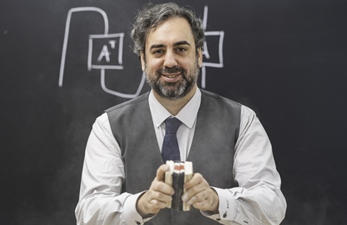 Un enseignant souriant présente des outils pédagogiques devant un tableau, illustrant des concepts technologiques innovants.
