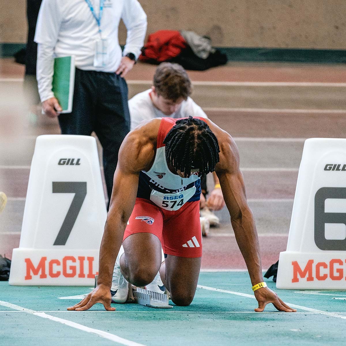 Athlète en position de départ sur la piste, concentré et prêt à s'élancer, avec des repères visibles pour la compétition.